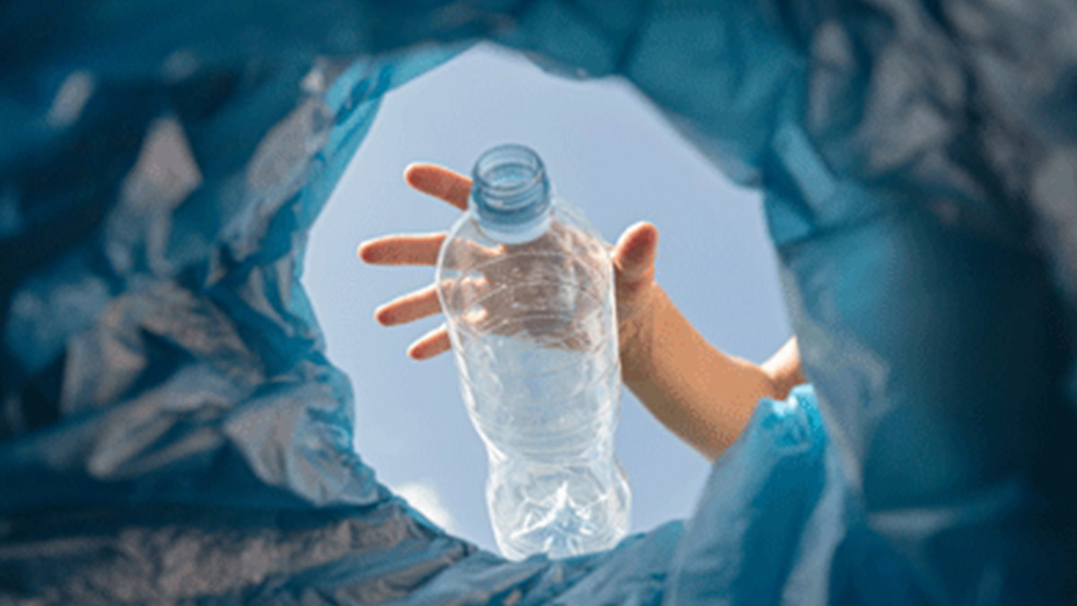 A hand letting go of a plastic water bottle in a trash can