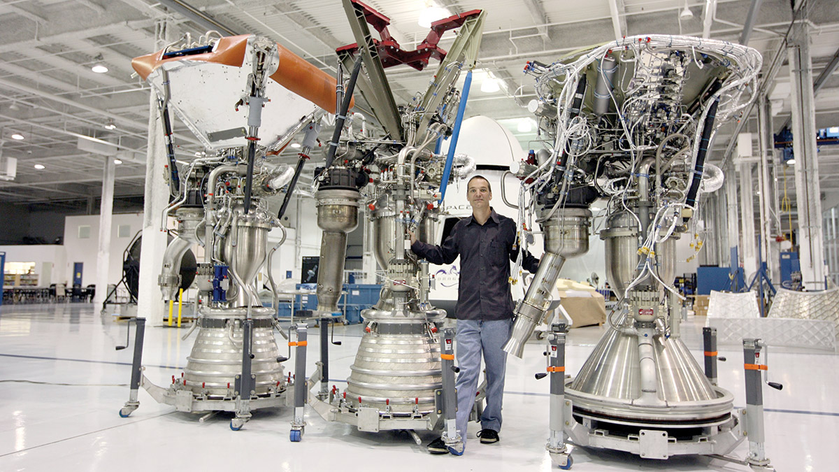 Tom Mueller poses with three rocket engines, which are nearly twice as tall as he is.