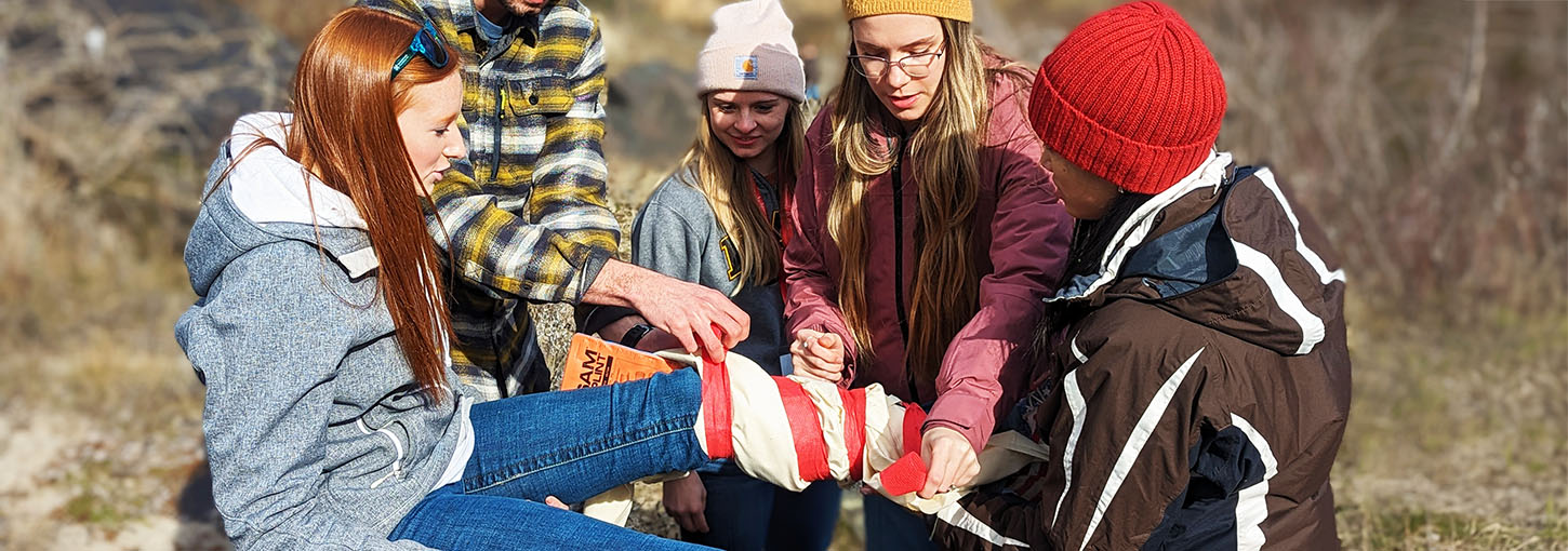 Idaho WWAMI students tie a leg brace around a volunteer victim during a medical simulation.