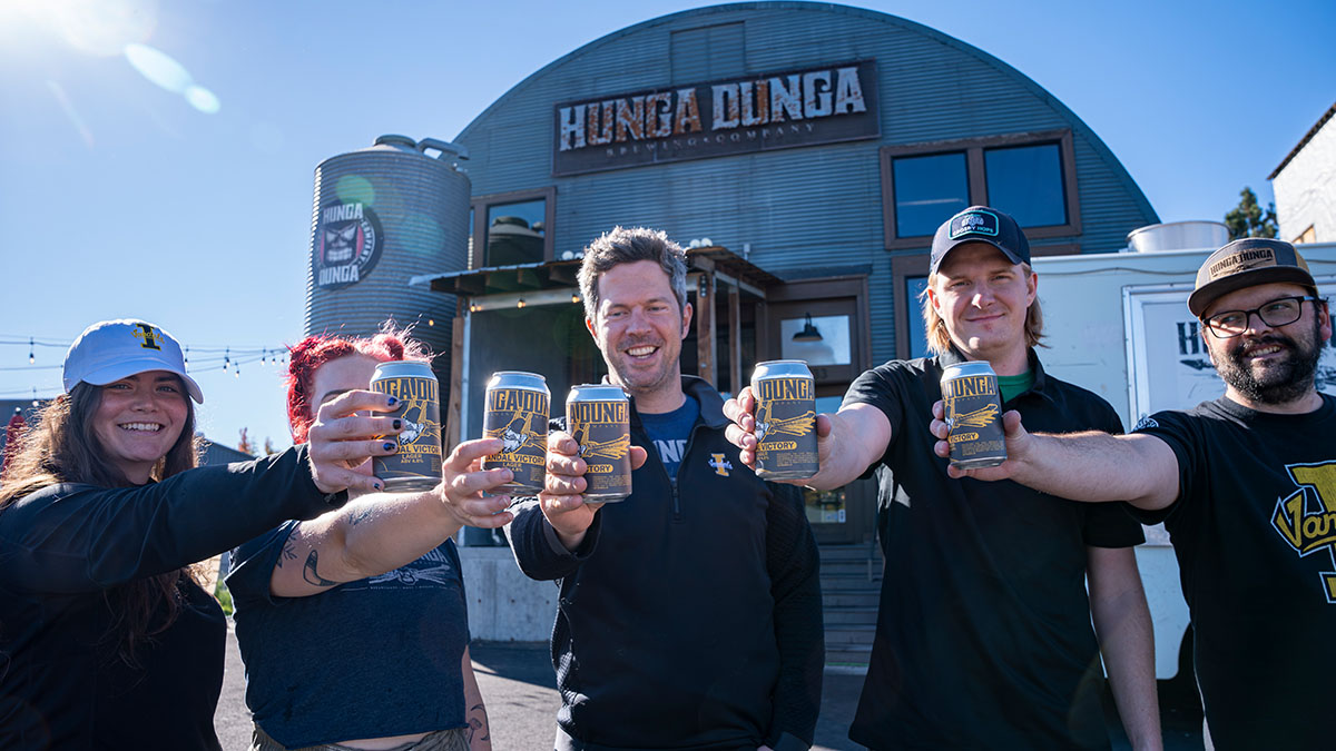 Two women and three men stand outside Hunga Dunga Brewing in Moscow each holding a black, gold and silver can of Vandal Victory Lager beer. 