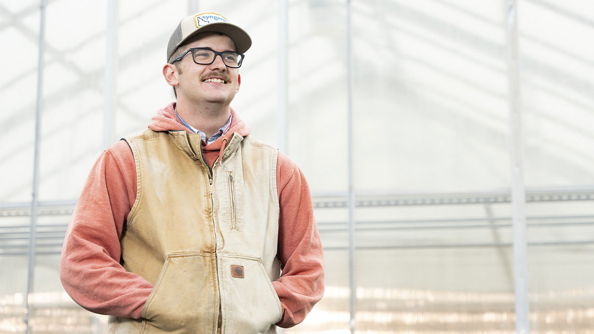 A man stands outside in front of a greenhouse.