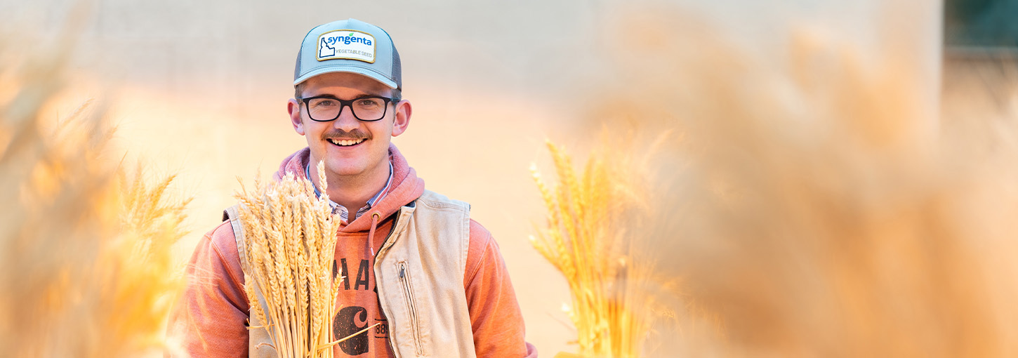 A man holds a bushel of wheat inside a greenhouse.