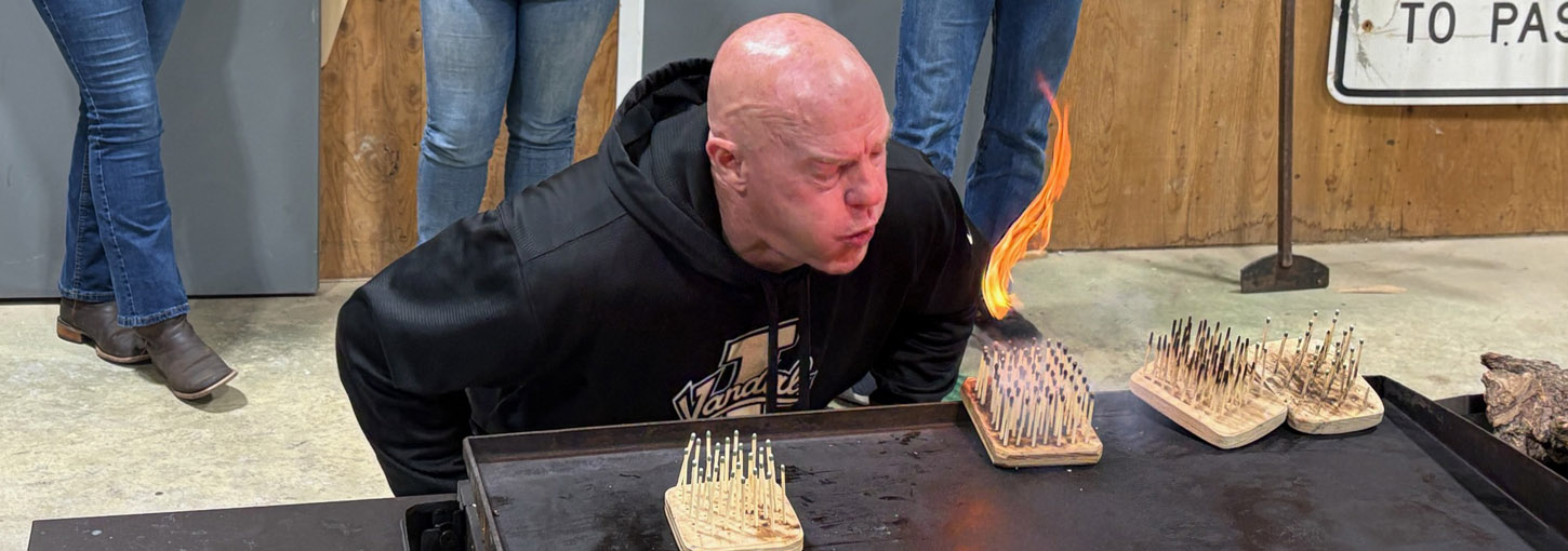 A large flame flares up from several matchsticks propped up in close proximity on a square block to mimic what happens when an overcrowded forest is ignited.