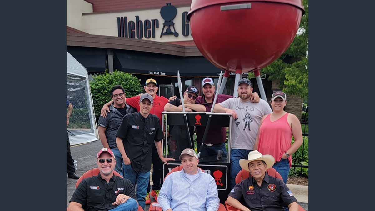 A group of men in front of Weber grill.