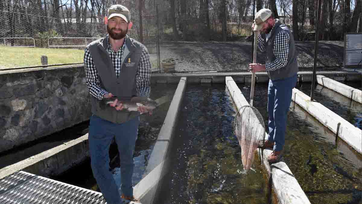 A man holding a trout and skimming waterway.
