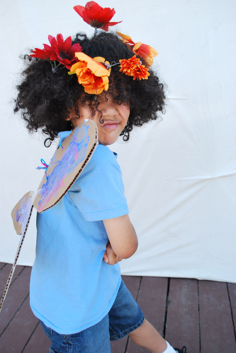 A child in costume with cardboard wings and flowers in his hair.