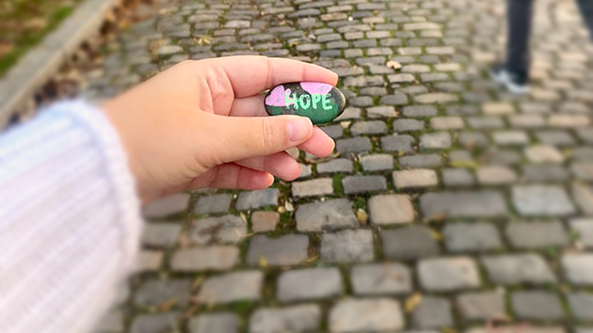 a girl holds a rock with the word HOPE on it on a cobblestone street in Europe