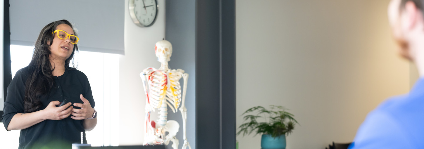 person standing and talking in a room with medical human skeleton in background