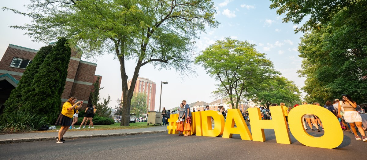 Two people taking a photo in front of a standing #UIDAHO sign on the street