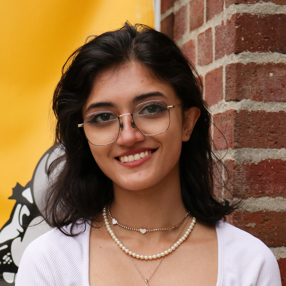 Nandani Singh smiles outdoors on campus, a brick building in the background with a banner featuring an illustration of Joe Vandal.