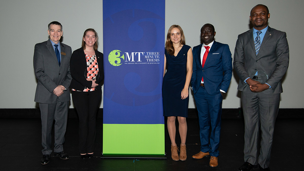 A group of people standing next to a "3MT" sign