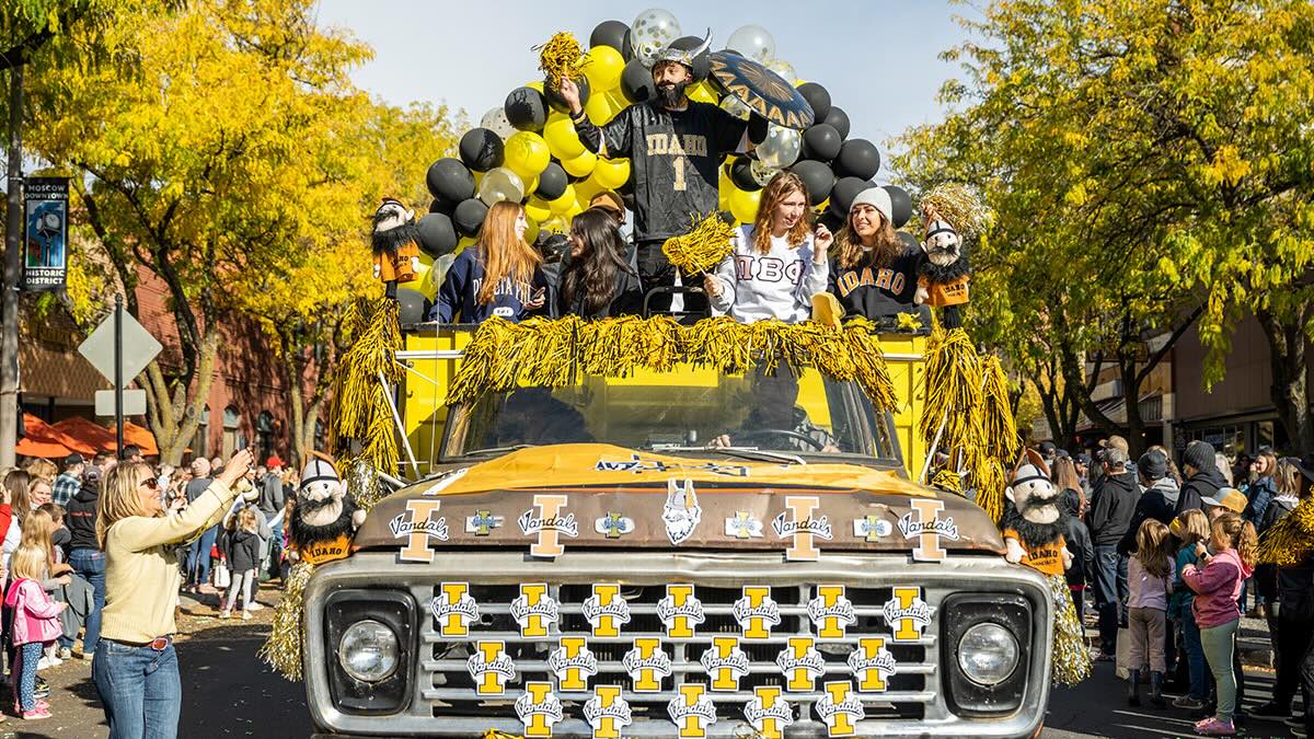 An old truck driving through downtown Moscow during the Homecoming parade with people taking pictures of it