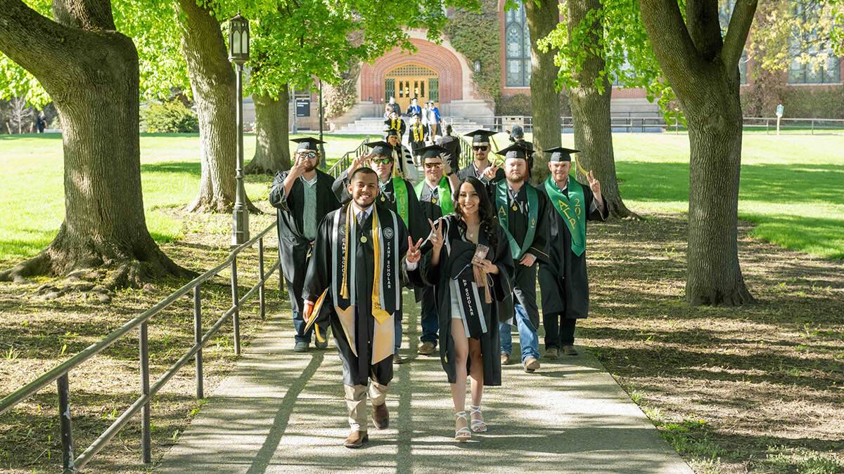University of Idaho students dressed in their cap and gown while walking on a path way
