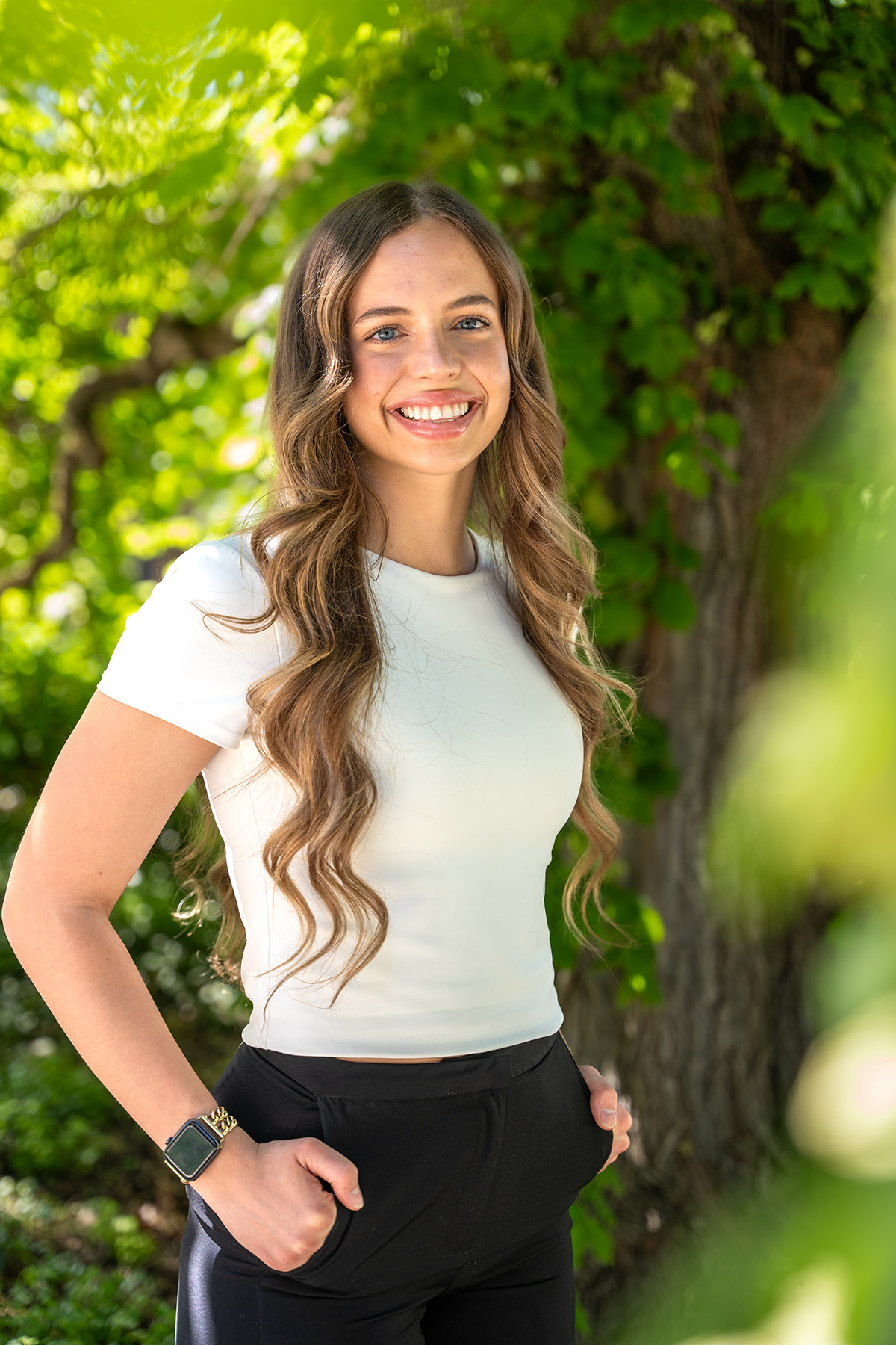 A woman in a white shirt stands in the shade of a tree.
