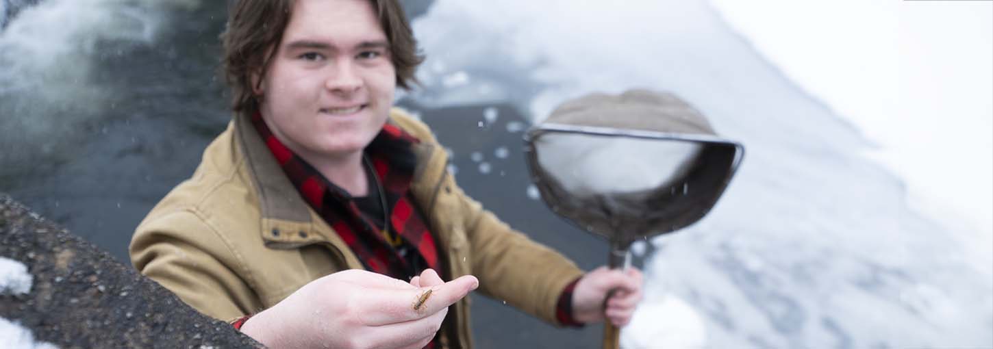 Student stands on ice flow in stream with a bug on their hand