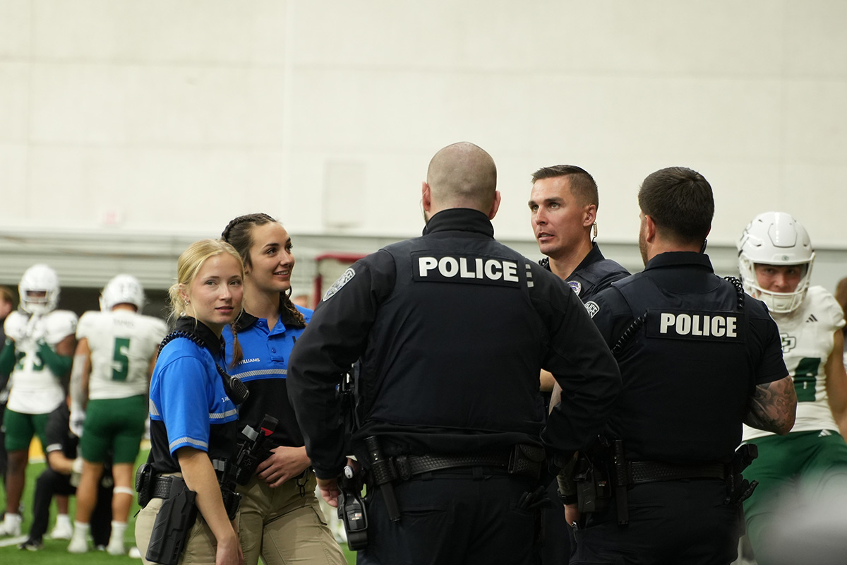 Two cadets meet with police at the sidelines of a football game.