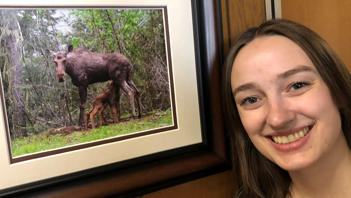 Smiling woman stands by a framed photograph of a moose.
