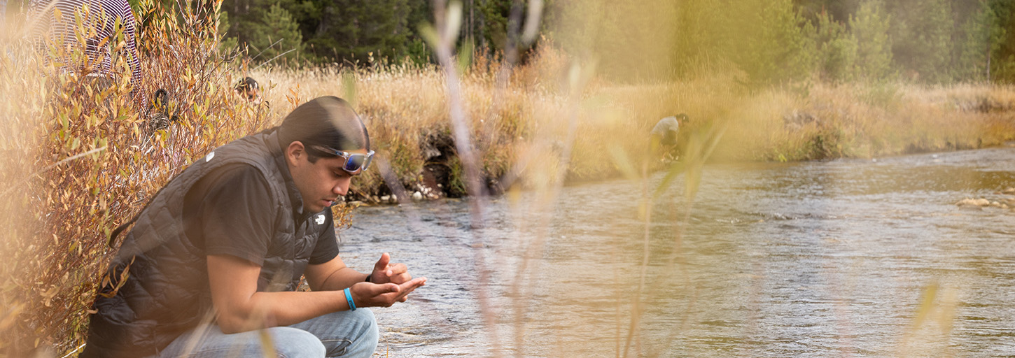 Man kneeling at river.