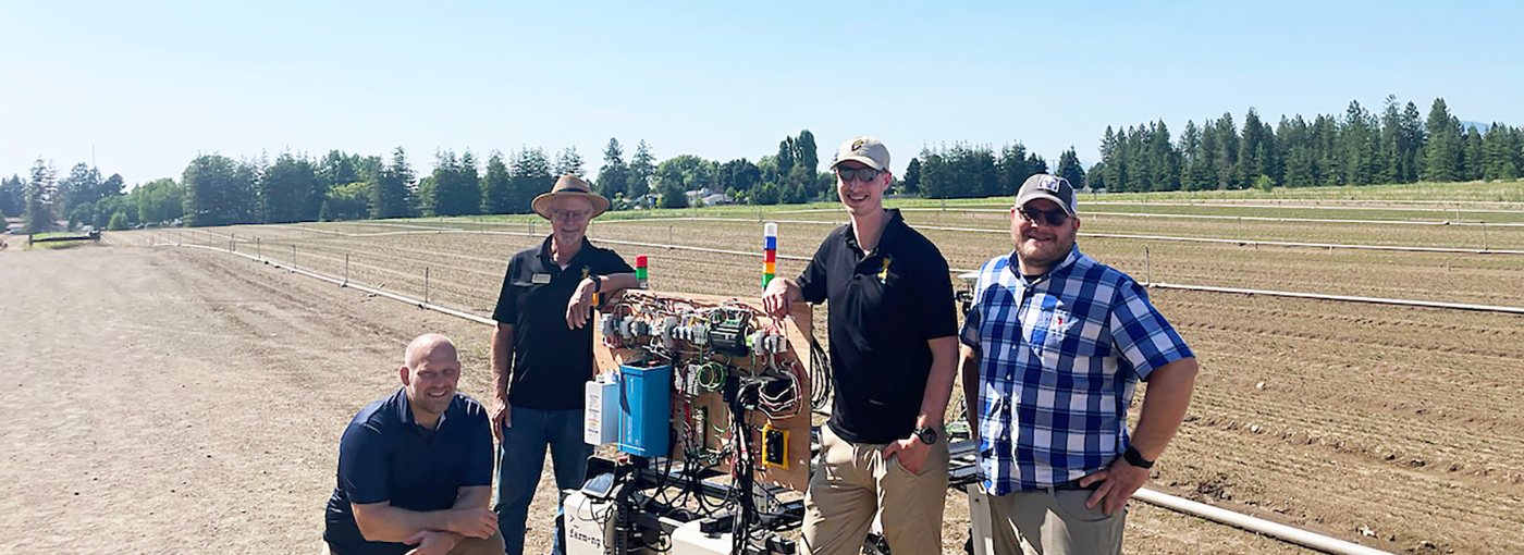 Four men pose with the weeding robot.