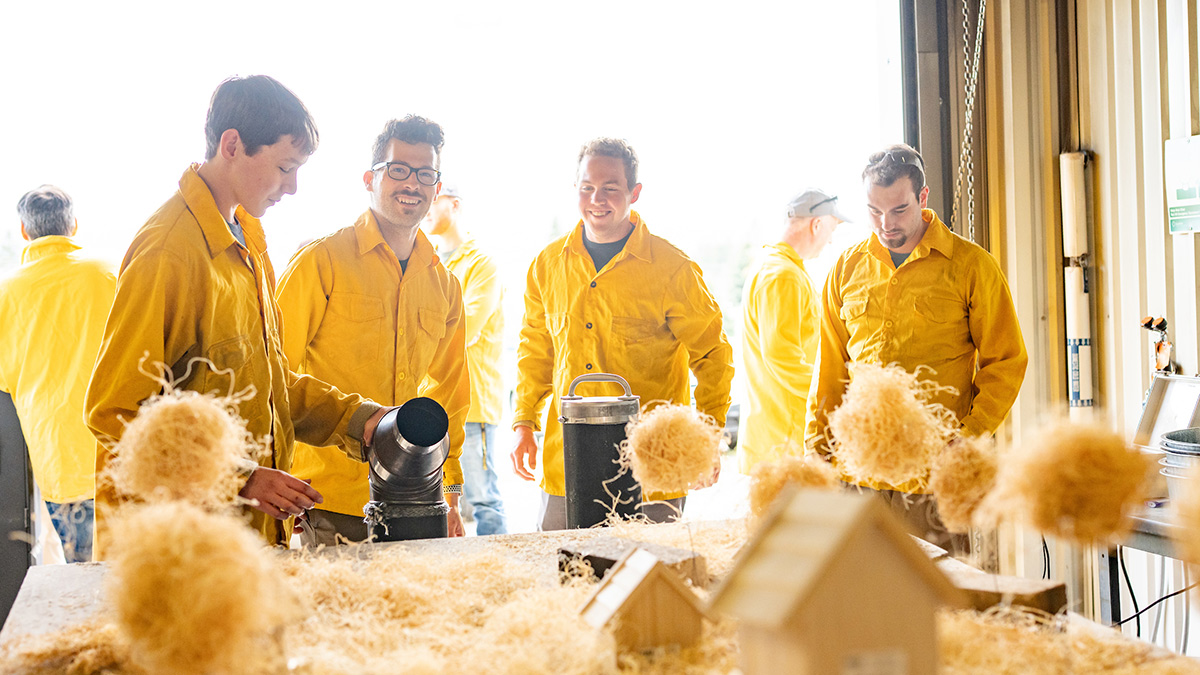 A team of four, all people wearing yellow, stand around a table of combustible props.